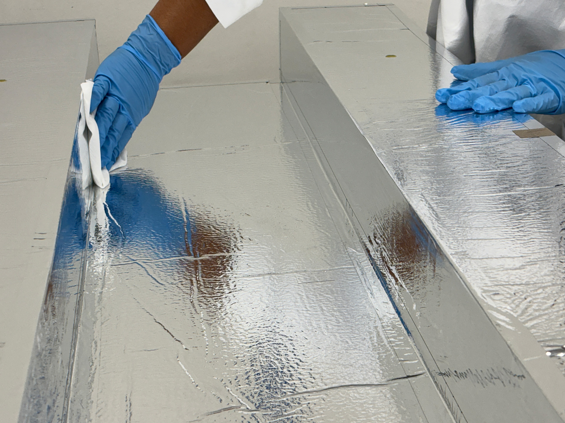 Pair of gloved hands working on an aerospace part assembly with mylar facing